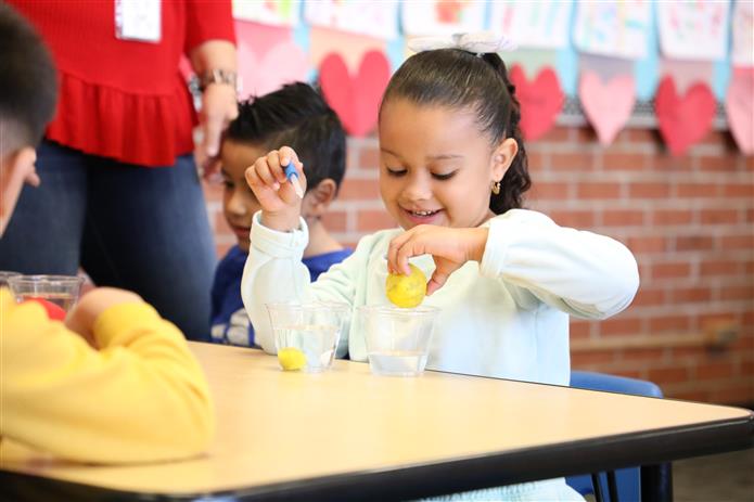 Image of 1 preschool student experimenting with clay and water while smiling